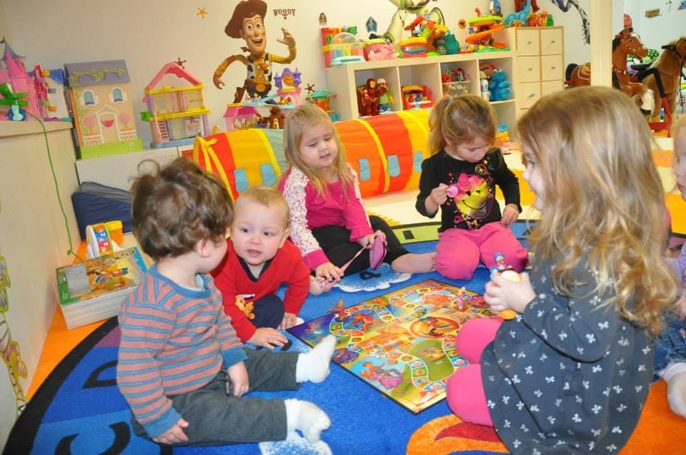 Kids gathered around a board game on the play rug