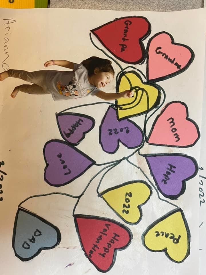 An overhead view of a child making a colorful Valentine's hearts art project