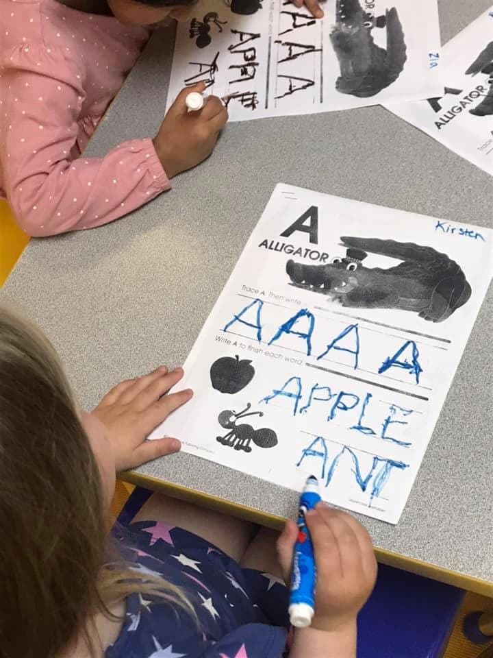 Two children practicing writing the letter A on alphabet worksheets