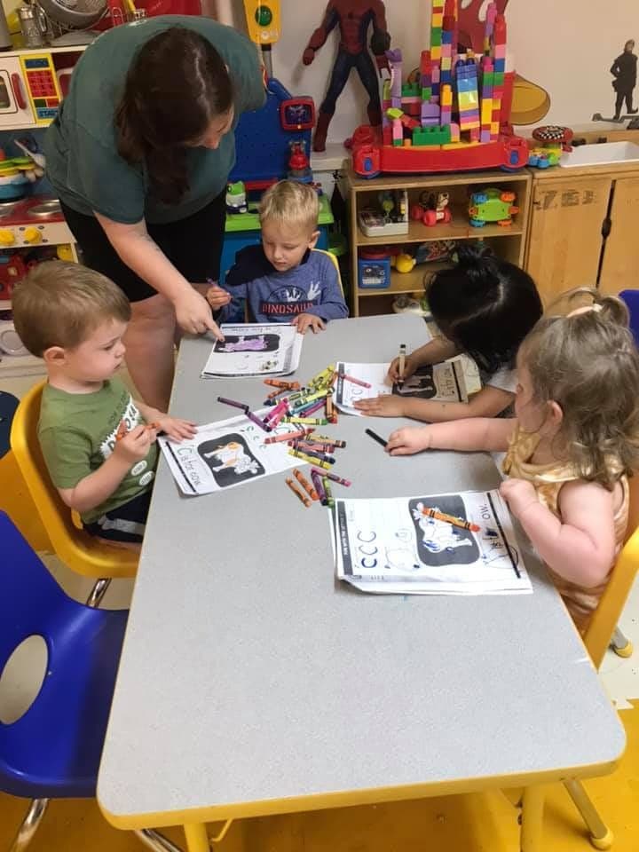 Preschoolers working on alphabet worksheets together with a teacher's help