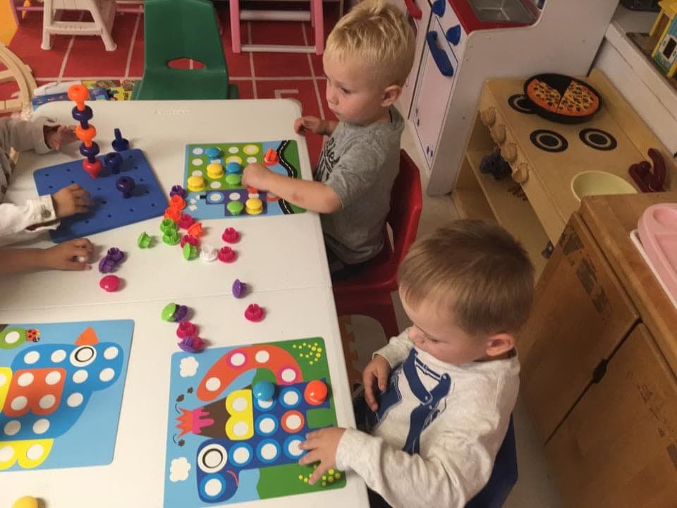 Two boys focused on a colorful peg-and-pattern learning toy
