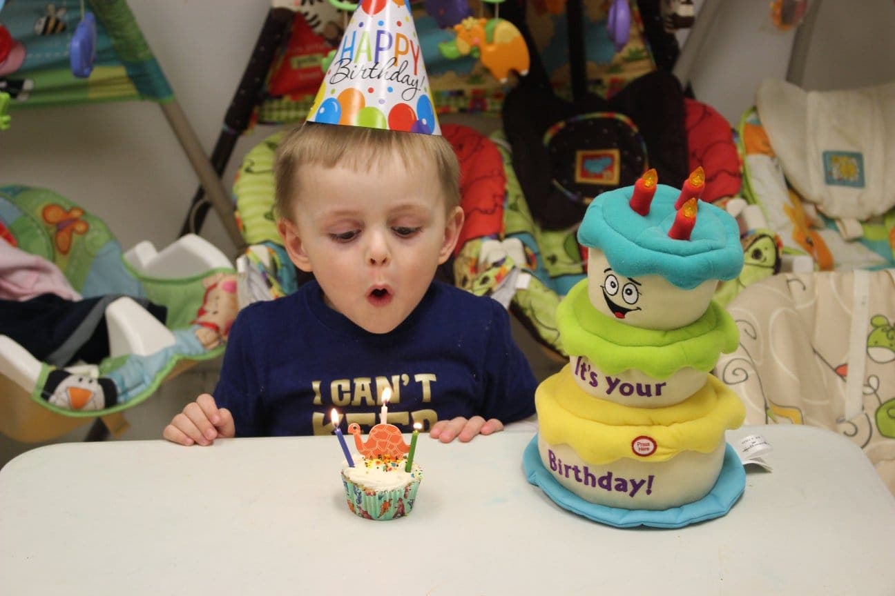 A toddler in a Happy Birthday hat blowing out candles on a cupcake