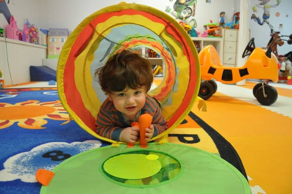 A toddler crawling out of a colorful play tunnel onto the playmat