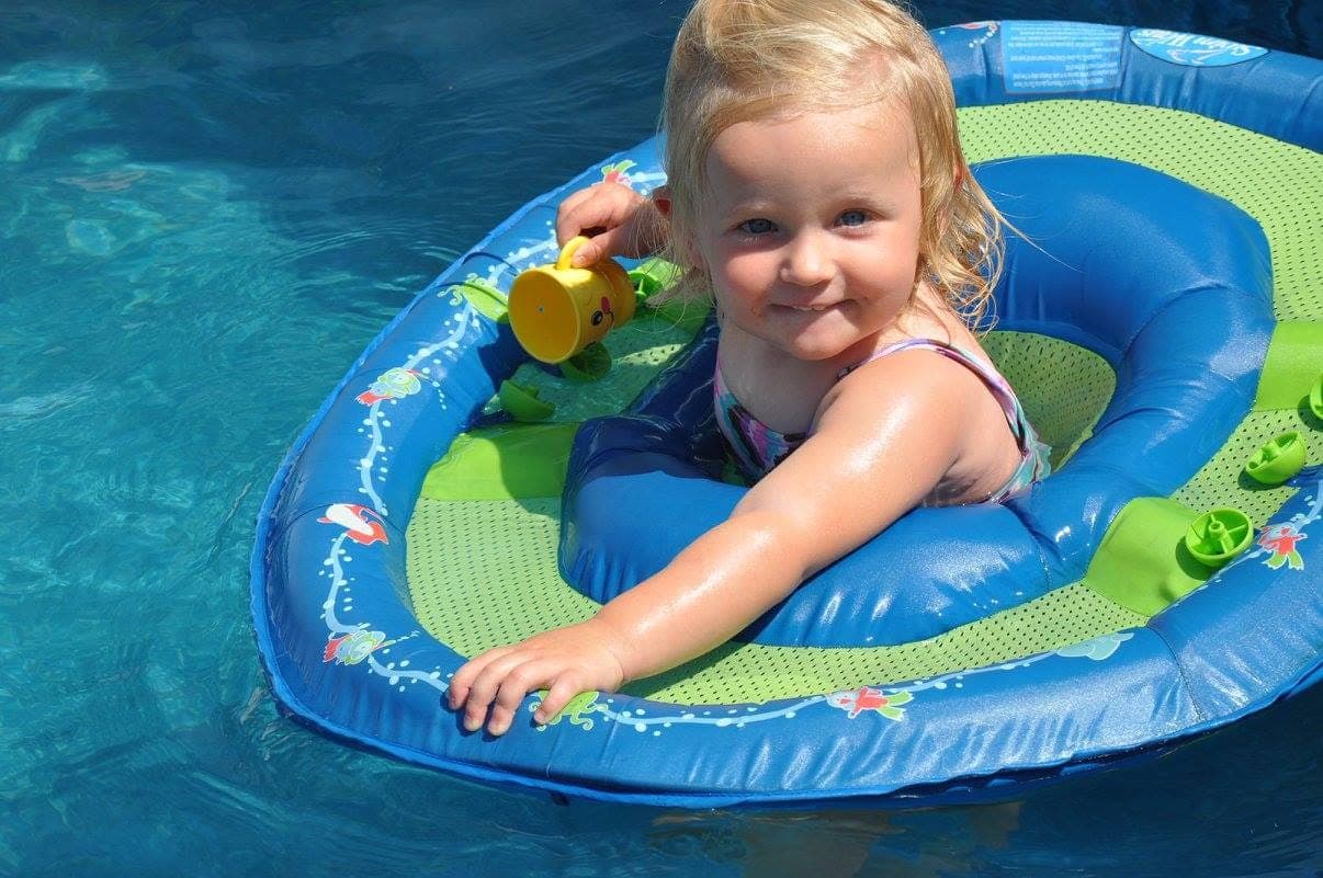 A smiling toddler in a baby pool float enjoying a sunny summer day