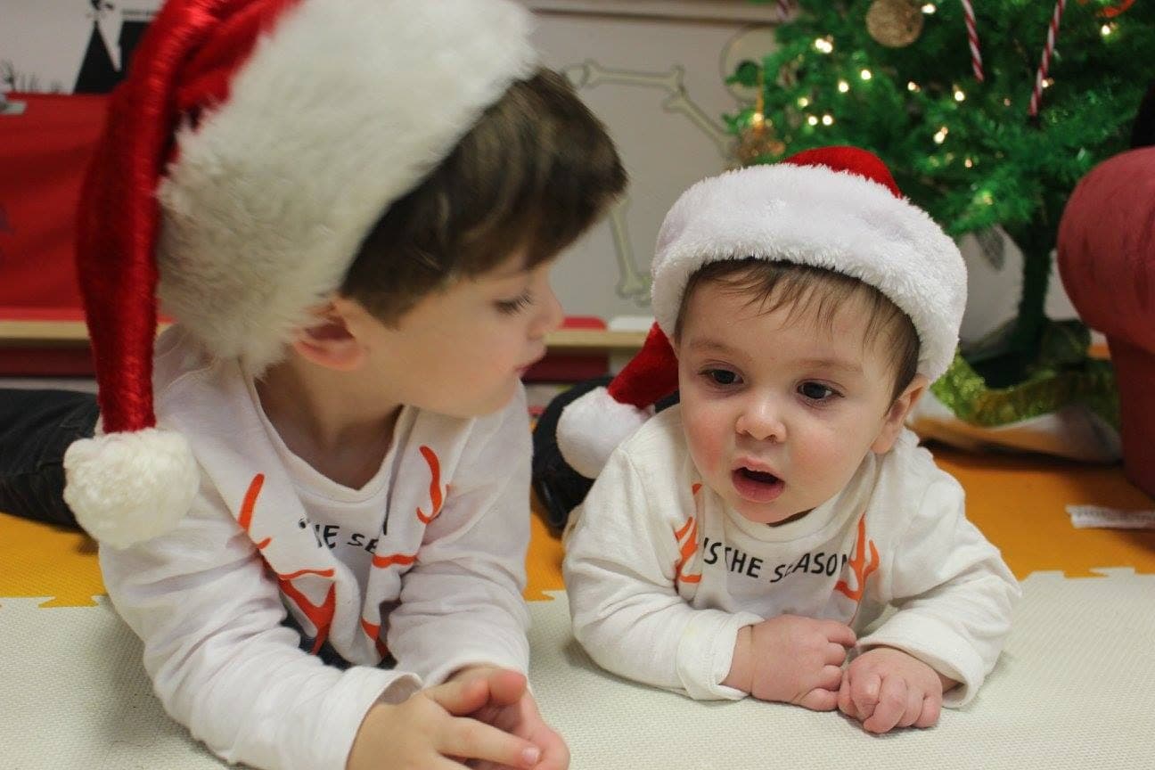 Two little ones in Santa hats side by side during the holidays at the playhouse