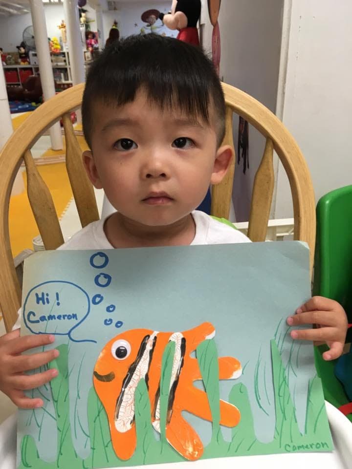 A preschooler proudly holding up his handmade clownfish art project