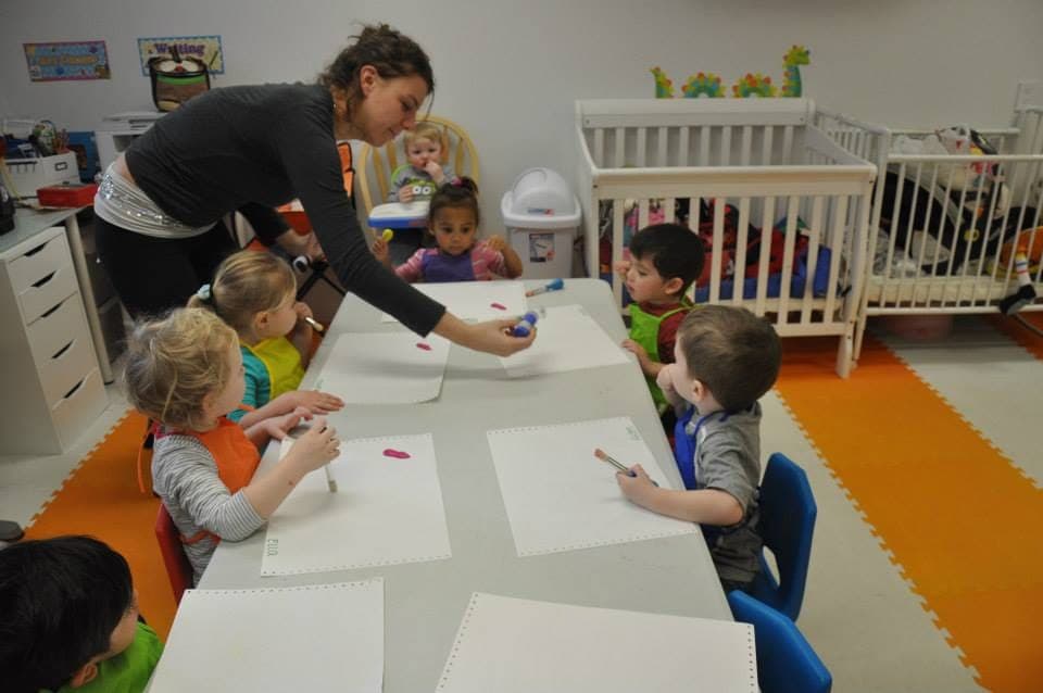 A teacher leading a painting project at a long table full of focused little artists