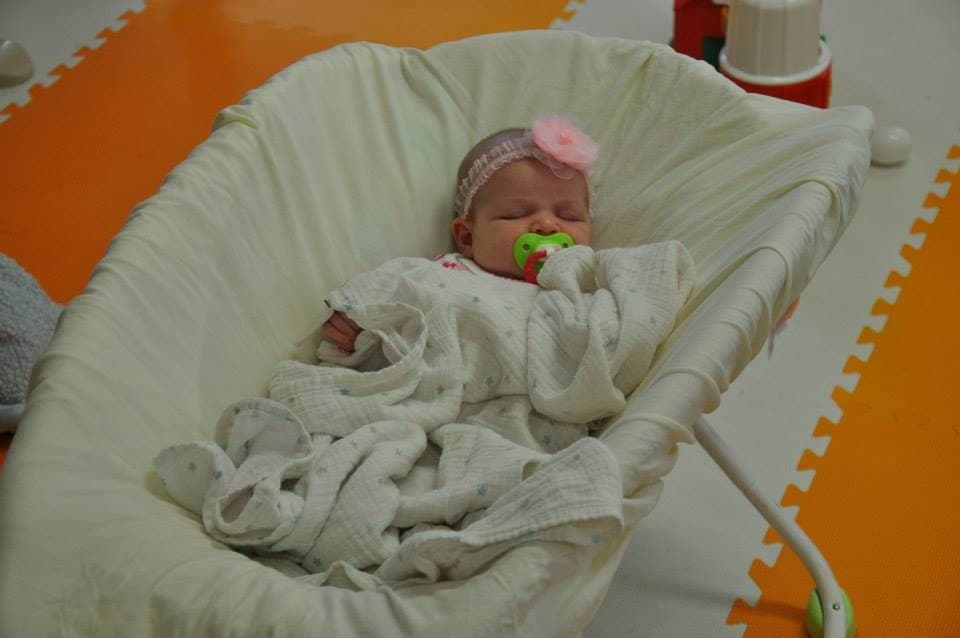 A peacefully sleeping baby swaddled in a soft white blanket in a cozy bouncer at Kelly's Kidz Playhouse