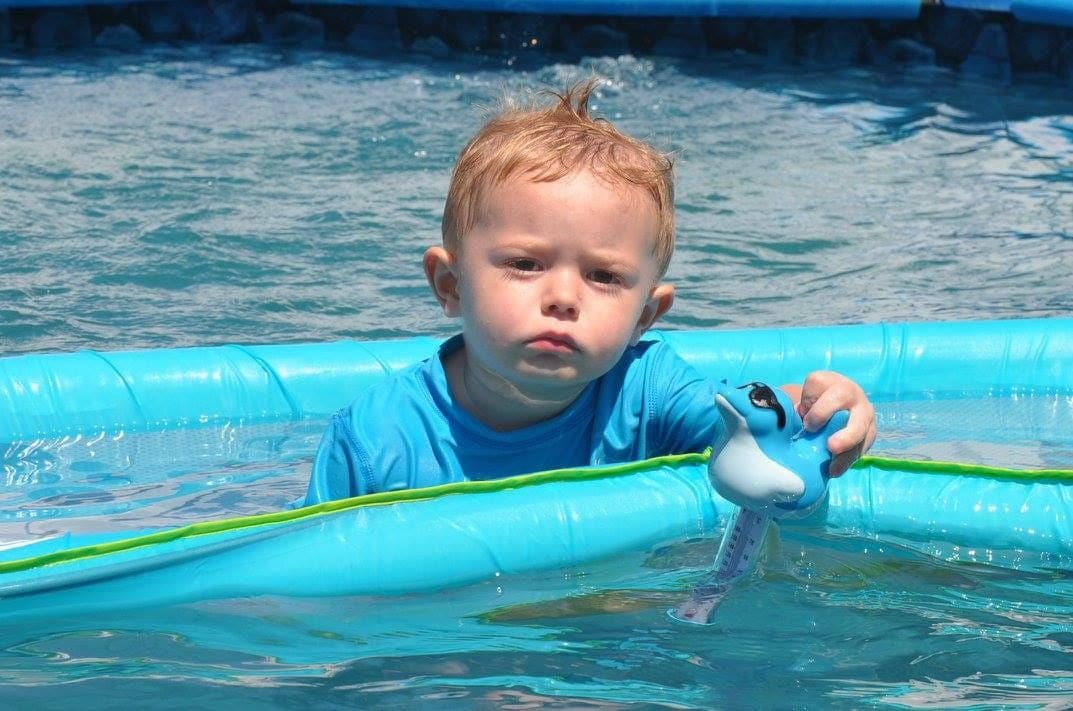 A focused toddler exploring a pool toy on a sunny summer day at Kelly's Kidz Playhouse